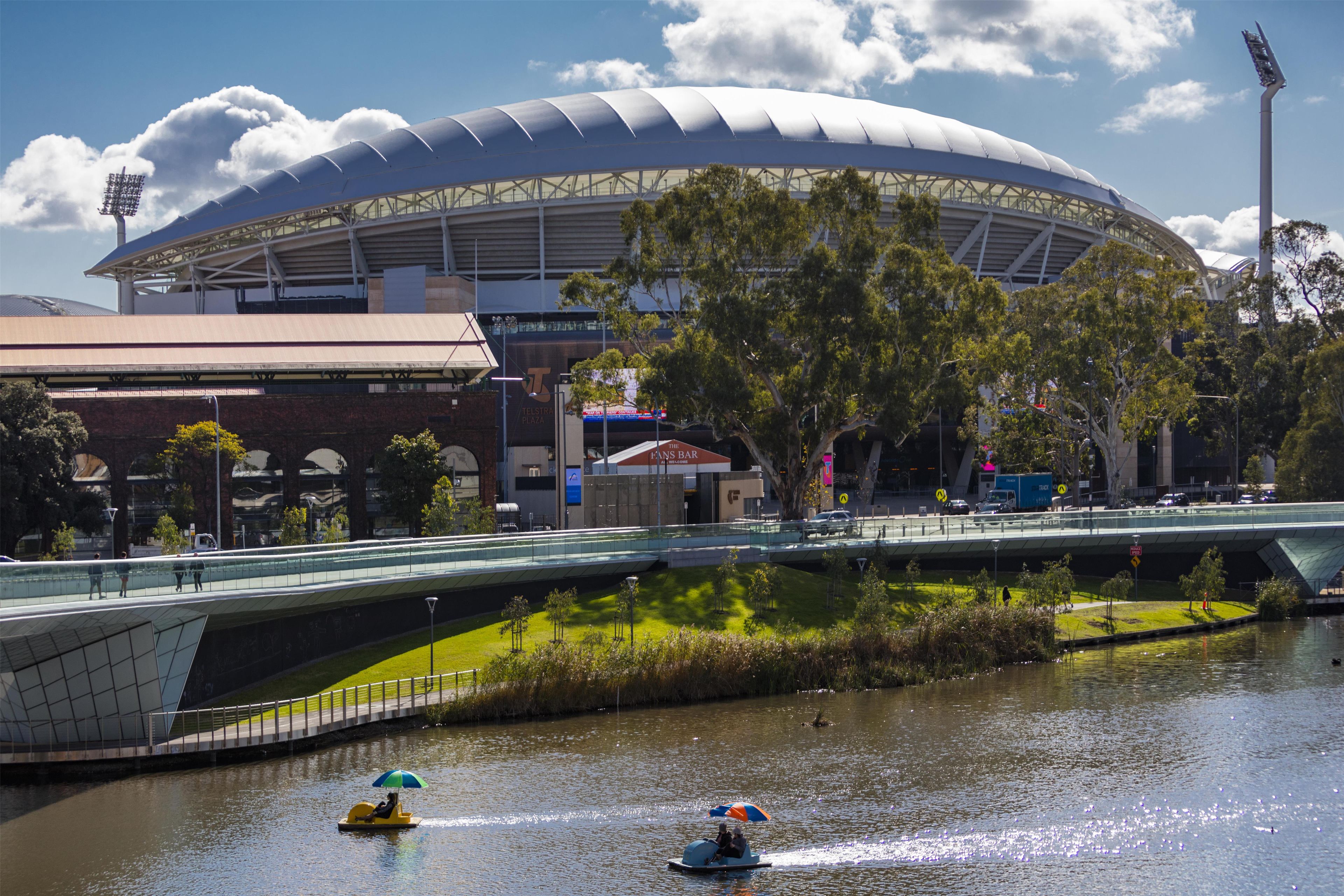 A stadium with a distinctive dome roof, a pedestrian bridge, and a body of water with boats.