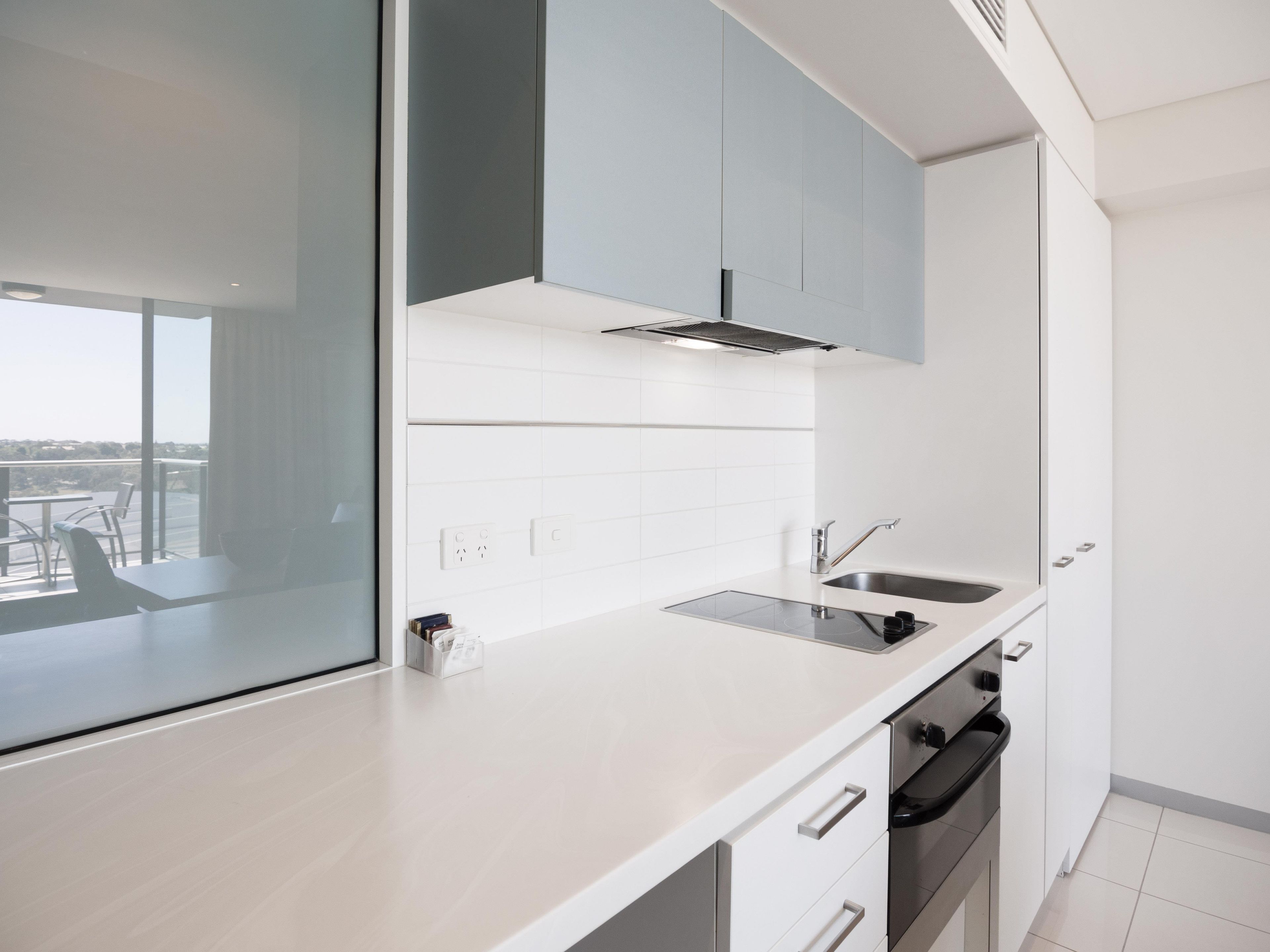 A modern kitchen with a built-in oven, a sink, and a window overlooking a balcony.