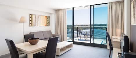 Ett modernt hotellrum med en matplats, en soffa, en TV och ett stort fönster med utsikt över staden.