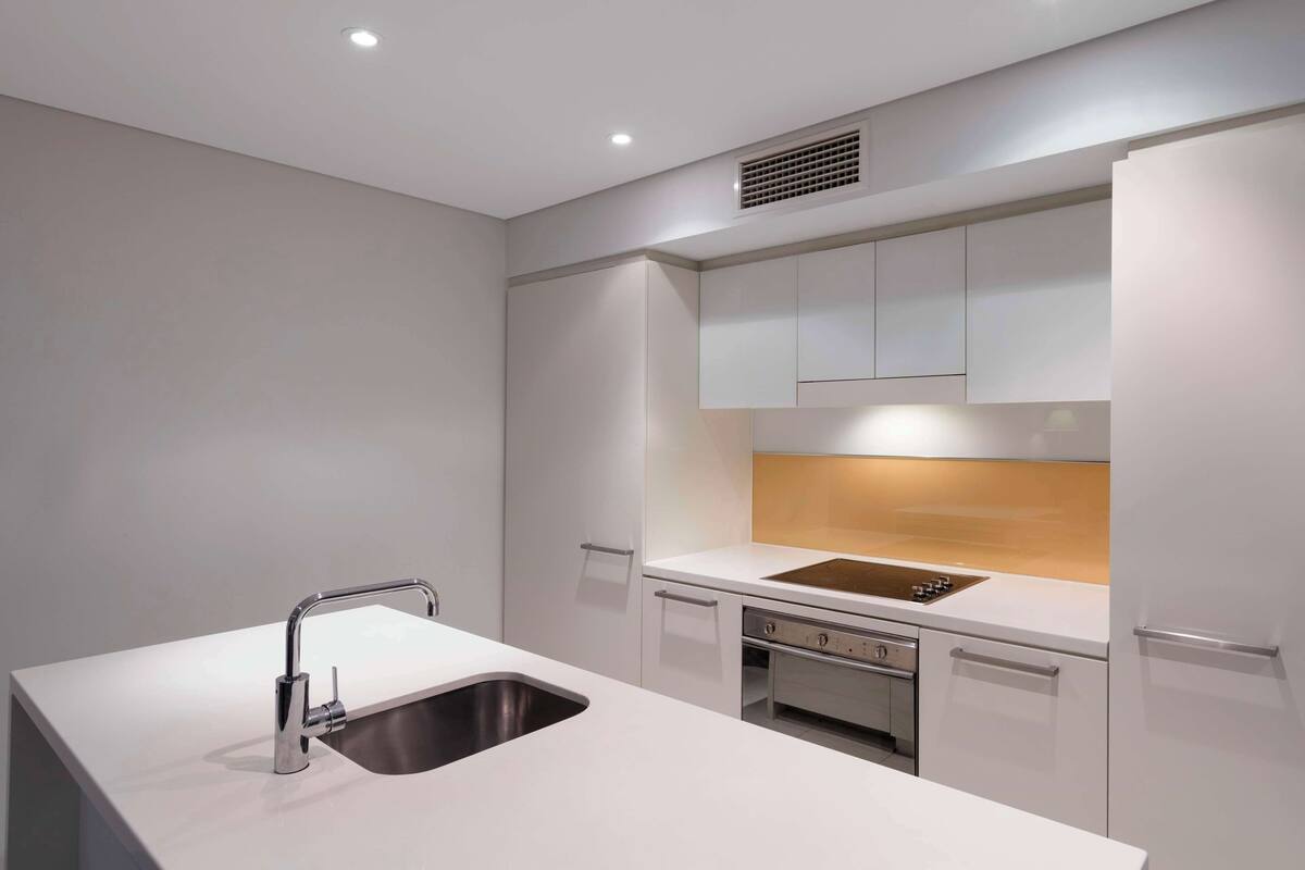 A modern kitchen with a stainless steel sink, white cabinetry, and a built-in oven.