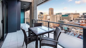 A balcony with a glass table and wicker chairs, offering a city view.