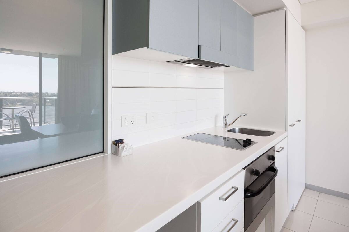 A modern kitchen with a built-in oven, a sink, and a window overlooking a balcony.