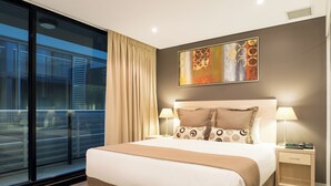 A modern hotel room with a large bed, a nightstand, a lamp, and a painting on the wall. - Oaks Adelaide Horizons Suites (Adelaide)