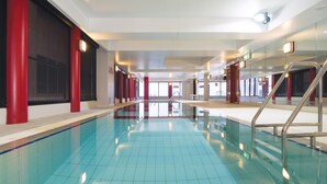 An indoor swimming pool with clear blue water, red pillars, and a tiled floor.