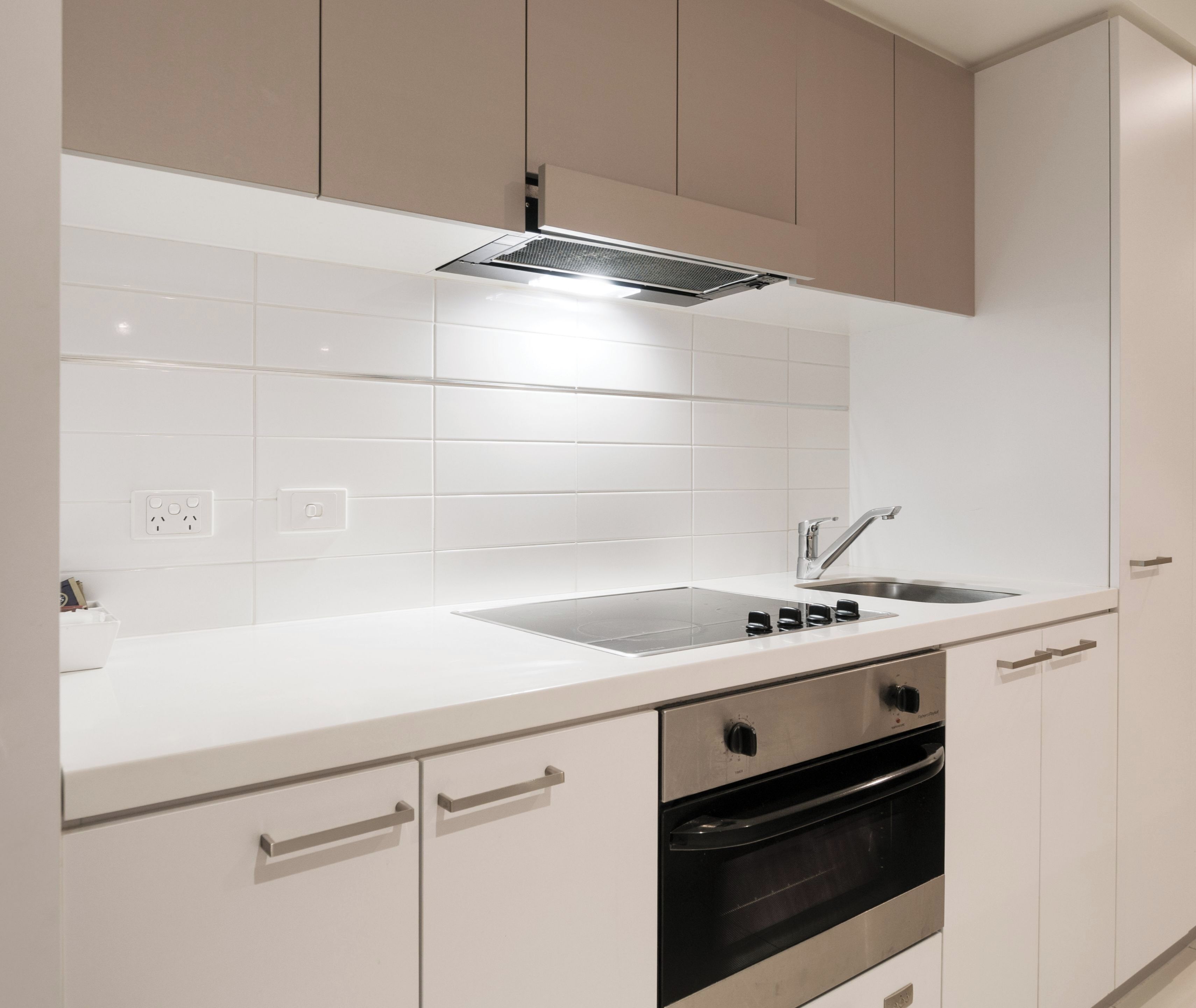 Een moderne keuken met witte kastjes, een RVS-spoelbak en een oven.