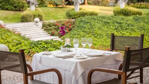 An outdoor dining area with a table set for two, surrounded by greenery and statues. - Cosmo Hotel Torri (Vimercate)