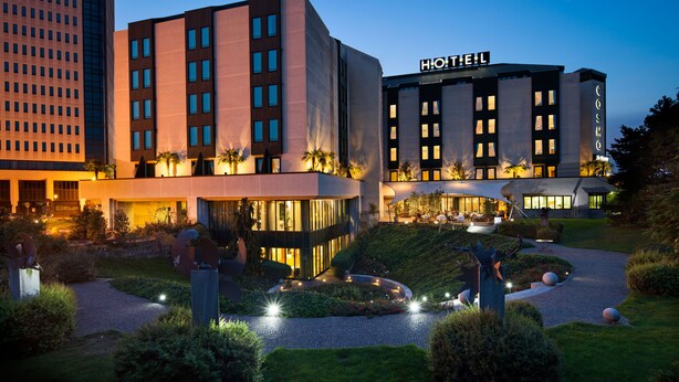 A modern hotel with a prominent 'HOTEL' sign, featuring a well-lit entrance and landscaped gardens. - Cosmo Hotel Torri (Vimercate)