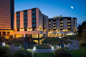 Un hotel moderno con un llamativo letrero que dice 'HOTEL', que cuenta con una entrada bien iluminada y jardines ajardinados.