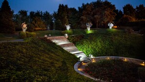 A nighttime garden with a stone pathway, sculptures, and a moonlit sky. - Cosmo Hotel Torri (Vimercate)