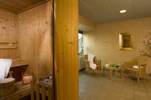A wooden sauna room with a bench, a small table with a candle, and a wicker chair. - Cosmo Hotel Torri (Vimercate)