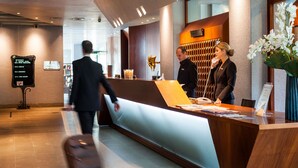 A hotel reception area with a wooden reception desk, a glass partition, and a signboard listing room types. - Cosmo Hotel Torri (Vimercate)