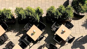 Un área de estar al aire libre con mesas cuadradas y sillas de ratán negro, rodeada de plantas en macetas.