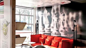 Un interior moderno con un sofá rojo, un cuadro mural de un tablero de ajedrez y una ventana con vistas a árboles.