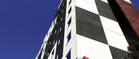A tall building with a checkered facade and a red 'ibis' sign.