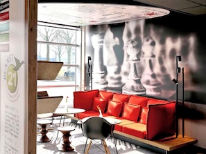 Een modern interieur met een rode bank, een muurschildering van een schaakbord en een raam met uitzicht op bomen en een auto.