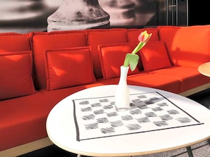 A red sofa with a white vase and a single tulip, a round table with a black and white patterned placemat, and a blurred background.