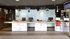 Zona de recepción de hotel con mostrador de mármol, múltiples monitores de ordenador y una pantalla digital que muestra tarifas y servicios.