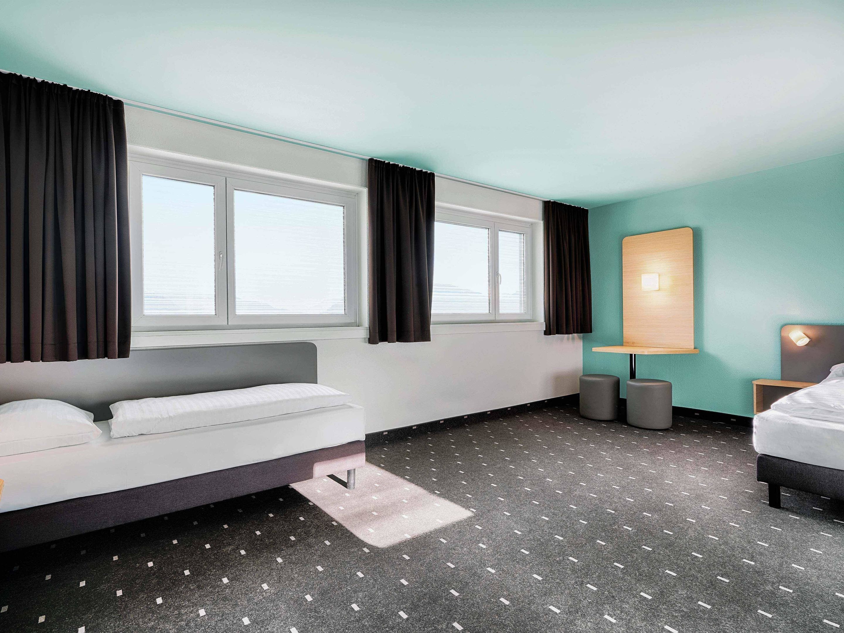 Una habitación de hotel moderna con cama, escritorio y un amplio ventanal con cortinas.
