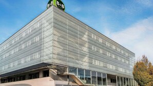 A modern B&B hotel with a distinctive glass facade and a prominent green logo on top. - B&B Hotel Salzburg-Nord (Salzburg)