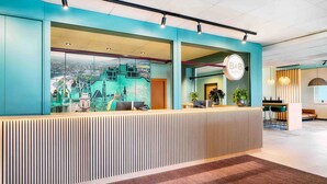 A modern hotel reception area with a large cityscape mural, a reception desk, and a seating area with a view of the city. - B&B Hotel Salzburg-Nord (Salzburg)
