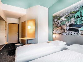 Una camera d'albergo con un letto, una scrivania, una sedia e una lampada a parete.