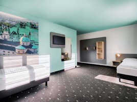 Una camera d'albergo moderna con un letto grande, una scrivania, una TV a parete e un murale raffigurante un panorama urbano.