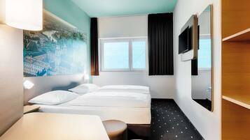 Ein Hotelzimmer mit Bett, Schreibtisch, Stuhl, einem kleinen Tisch, einem Fernseher und einem Fenster mit Vorhängen.