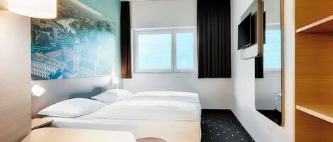 Une chambre d’hôtel comprenant un lit, un bureau, une chaise, une petite table, un téléviseur et une fenêtre avec des rideaux.