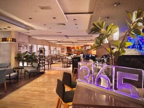 A modern hotel lobby with a wooden floor, seating areas, a Nespresso station, and a large illuminated number display. - Hotel Novotel Santiago Vitacura (Santiago)