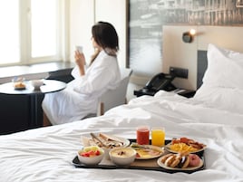 Una habitación de hotel con cama, bandeja de desayuno y una persona usando un teléfono.