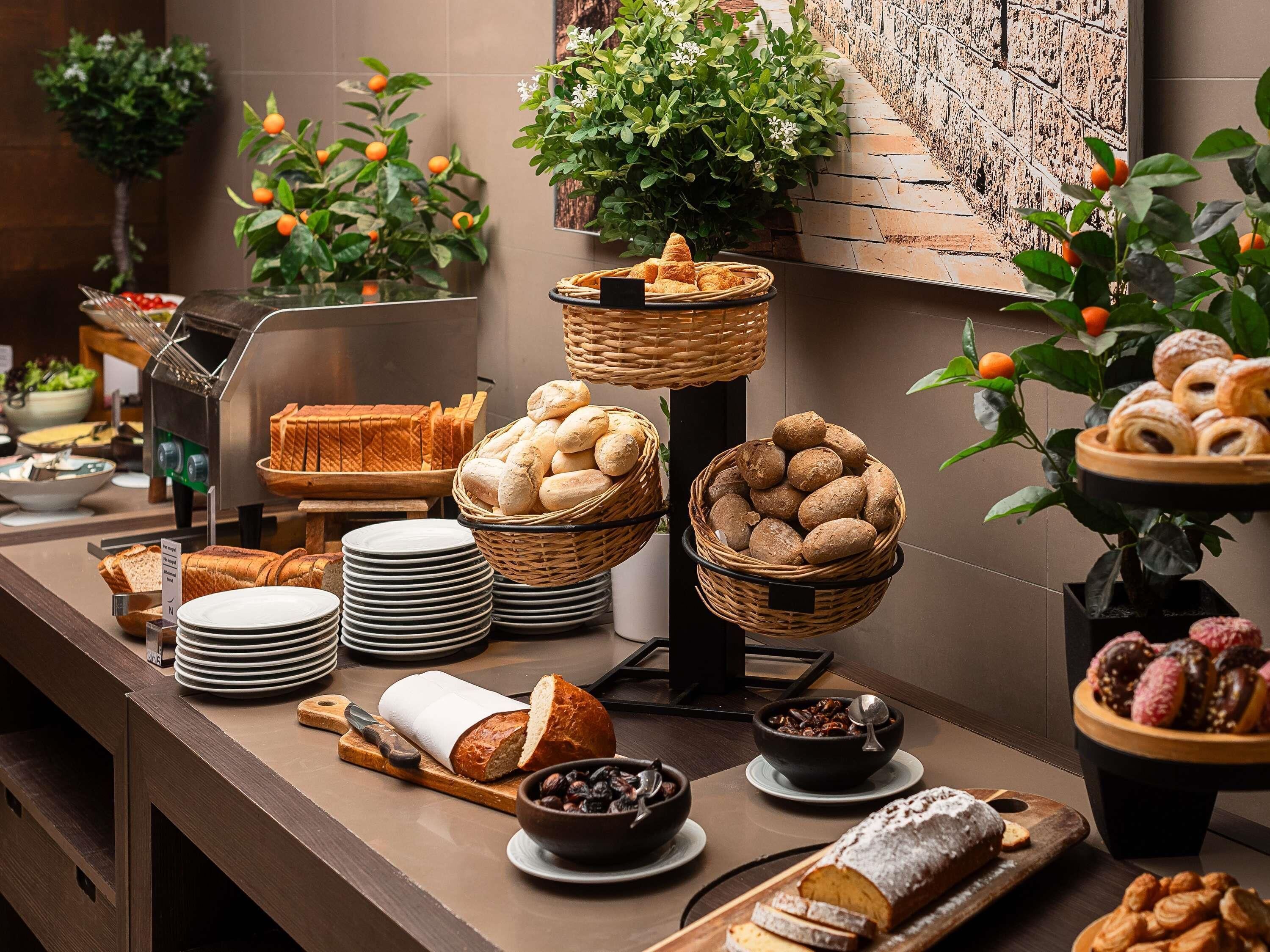 Mesa de buffet con pan, bollería y una planta.