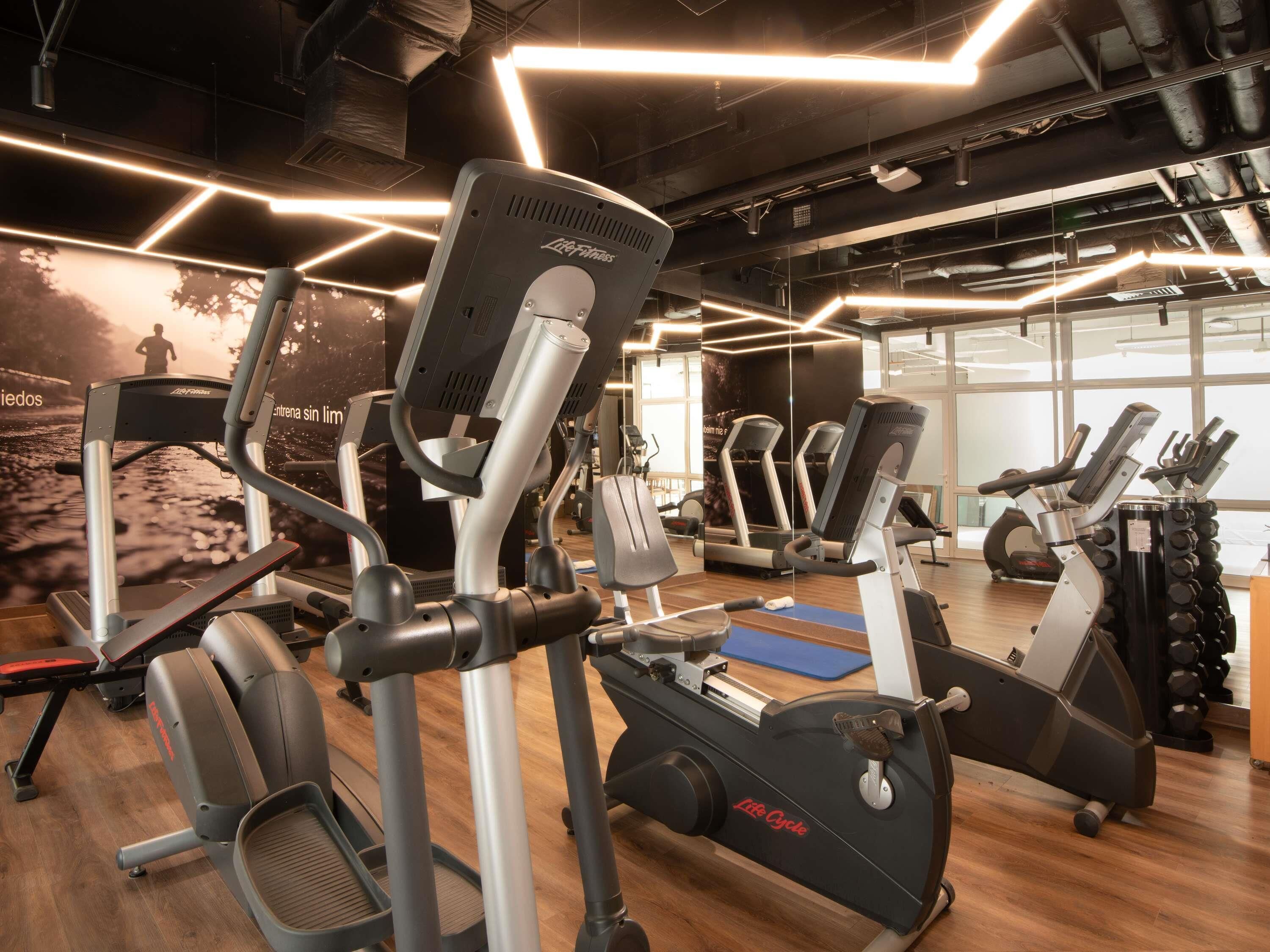 Uma academia com equipamentos de cardio, aparelhos de musculação e espelhos.