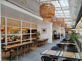 Un restaurante con techos altos, mobiliario de mimbre y un cerramiento de vidrio.