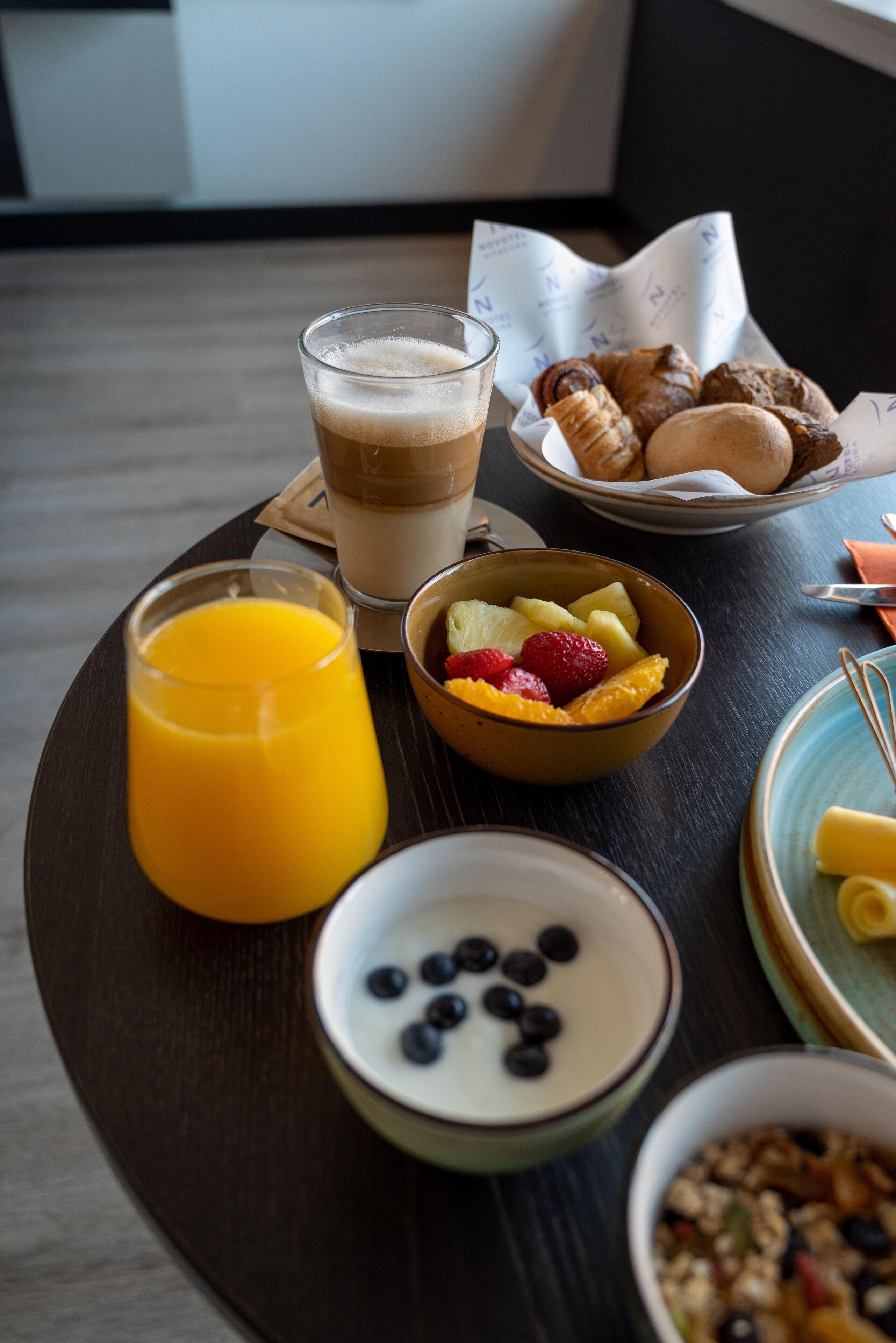 Ett frukostbricka med ett glas apelsinjuice, en skål med frukt, en skål med yoghurt och blåbär, en tallrik med croissanter och en kopp kaffe.