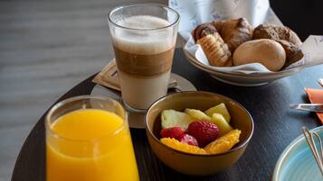 Ett frukostbricka med ett glas apelsinjuice, en skål med frukt, en skål med yoghurt och blåbär, en tallrik med croissanter och en kopp kaffe.