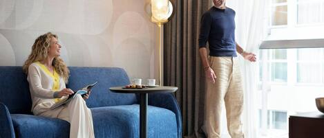 A room with a blue sofa, a small round table with cups and a plate, and a tall floor lamp.