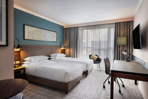 Habitación de hotel con dos camas, un escritorio, una silla, un televisor y una ventana con cortinas.