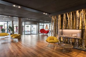 Un vestíbulo amplio con suelo de madera, sillas modernas amarillas, una silla roja y una pantalla montada en la pared.