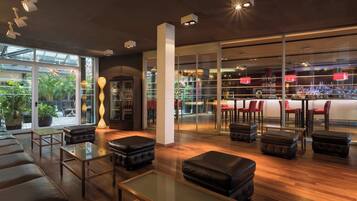 A modern lounge area with leather seating, a glass coffee table, and a bar area visible through glass doors.