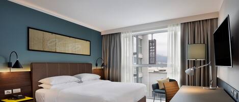 A hotel room with a large bed, a desk, a chair, a TV, and a window with curtains.