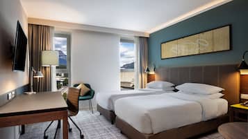A hotel room with a bed, a desk, a chair, and a view of the mountains.