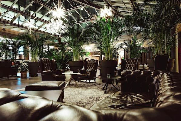 A spacious indoor area with leather sofas, armchairs, and a large potted plant.