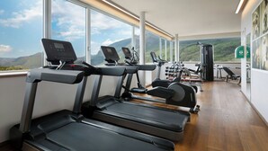 A gym with treadmills, exercise bikes, and weight machines, large windows with a mountain view. - Four Points by Sheraton Bolzano (Bolzano)