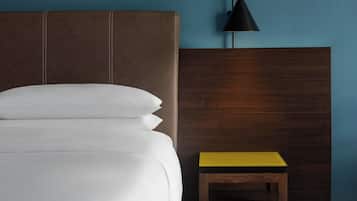 A bed with white linens, a wooden headboard, a small wooden nightstand with a yellow top, and a black pendant lamp.