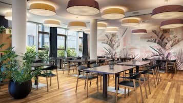 Interior moderno de restaurante con mesas de madera, sillas negras e iluminacion cenital.