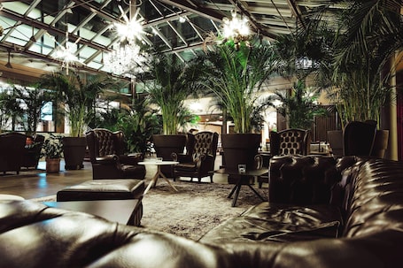 A spacious indoor area with leather sofas, armchairs, and a high ceiling with natural light.