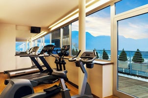 Un gimnasio con cintas de correr y elípticas, amplias ventanas con vistas a la montaña, y una terraza de madera en el exterior.