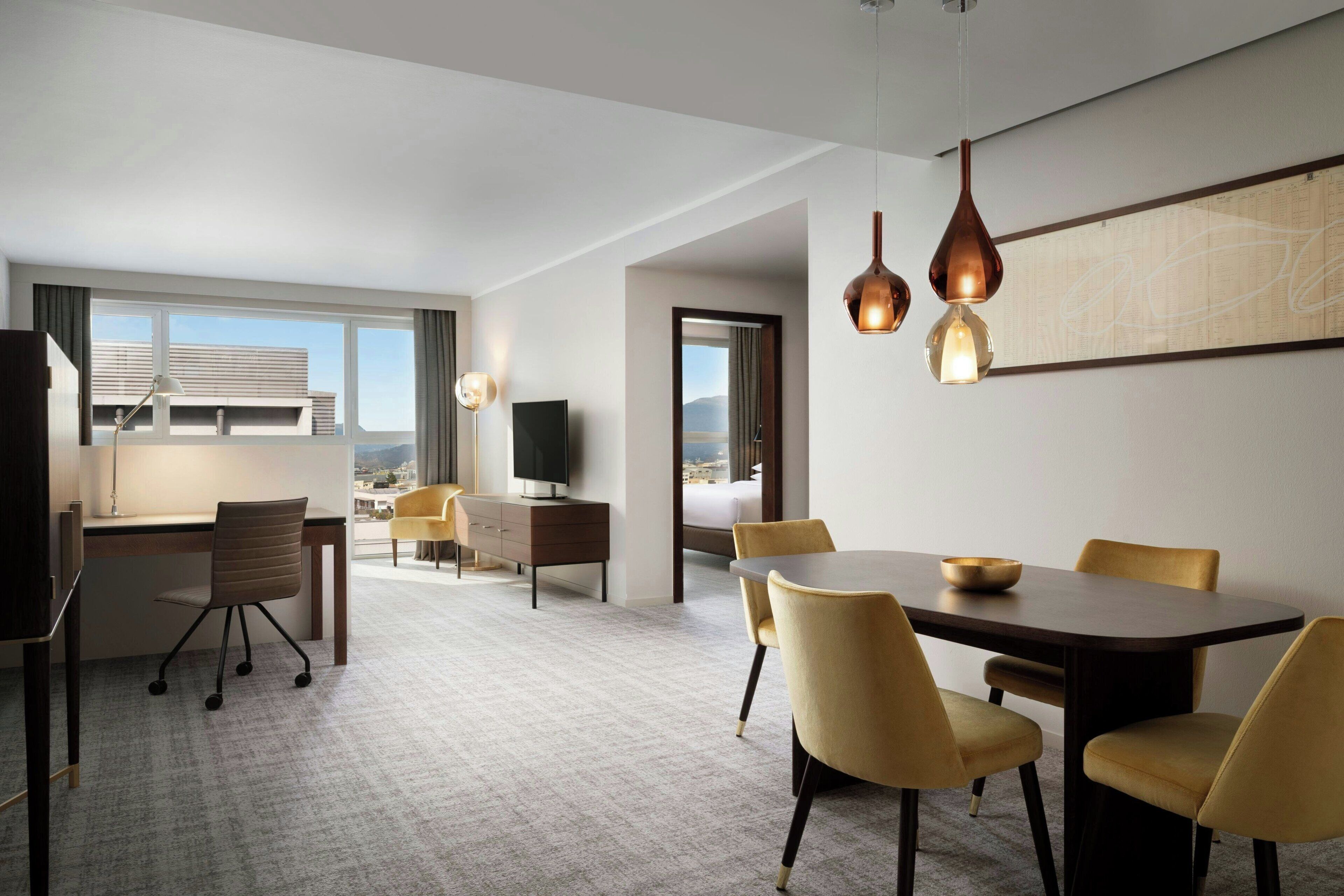 Habitación de hotel con comedor, escritorio, televisor y vista a la ciudad.