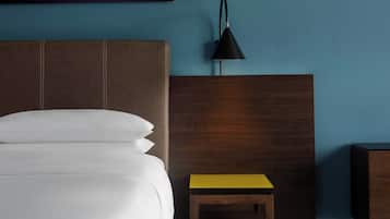 Ein Bett mit weißer Bettwäsche, ein hölzerner Kopfteil, ein kleiner Nachttisch mit gelber Oberfläche und eine schwarze Schreibtischlampe.