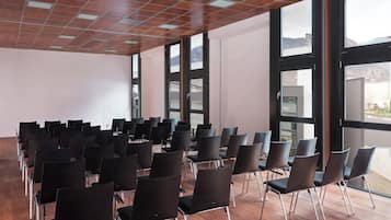 Ein Konferenzraum mit Reihen von Stühlen, großen Fenstern und einer Holzbalkendecke.